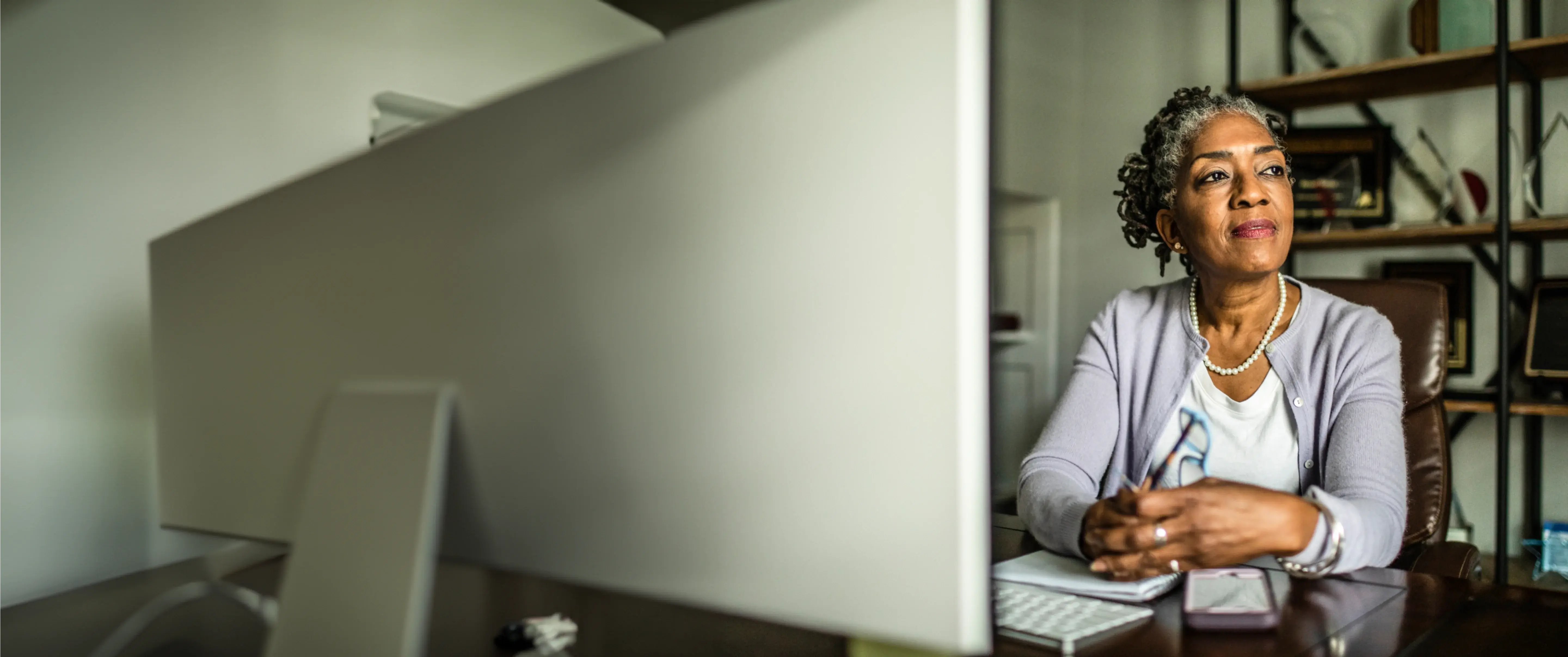 Porträt einer älteren Frau am Computer, die ihren Blick schweifen lässt