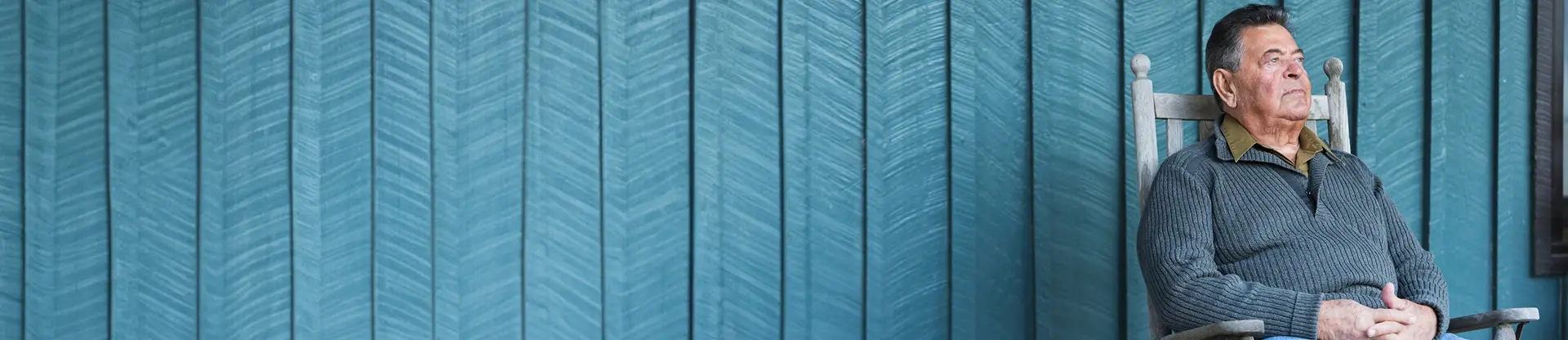 An elderly man sitting on a bench outside.