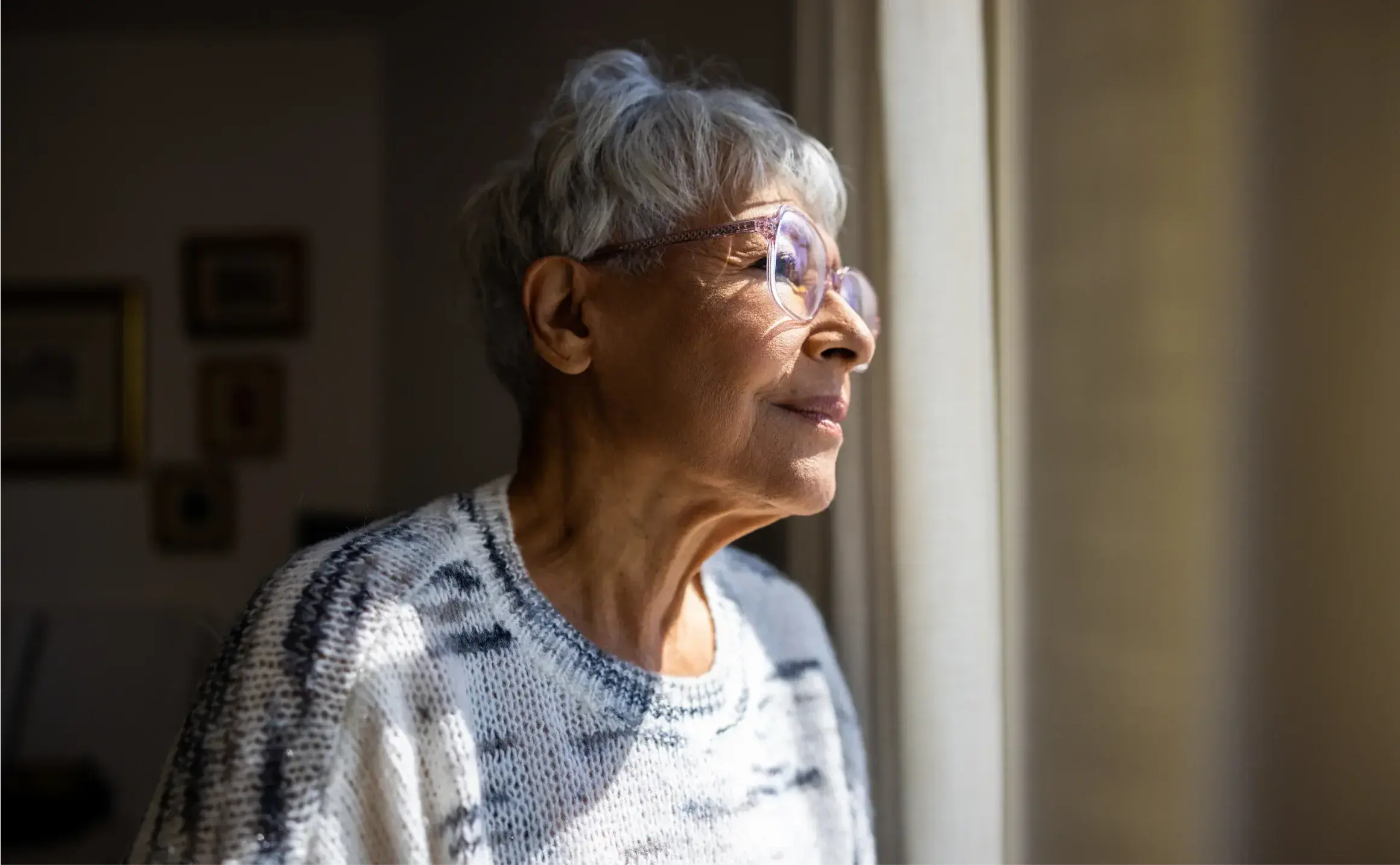 An elderly woman looking out the window of her house.