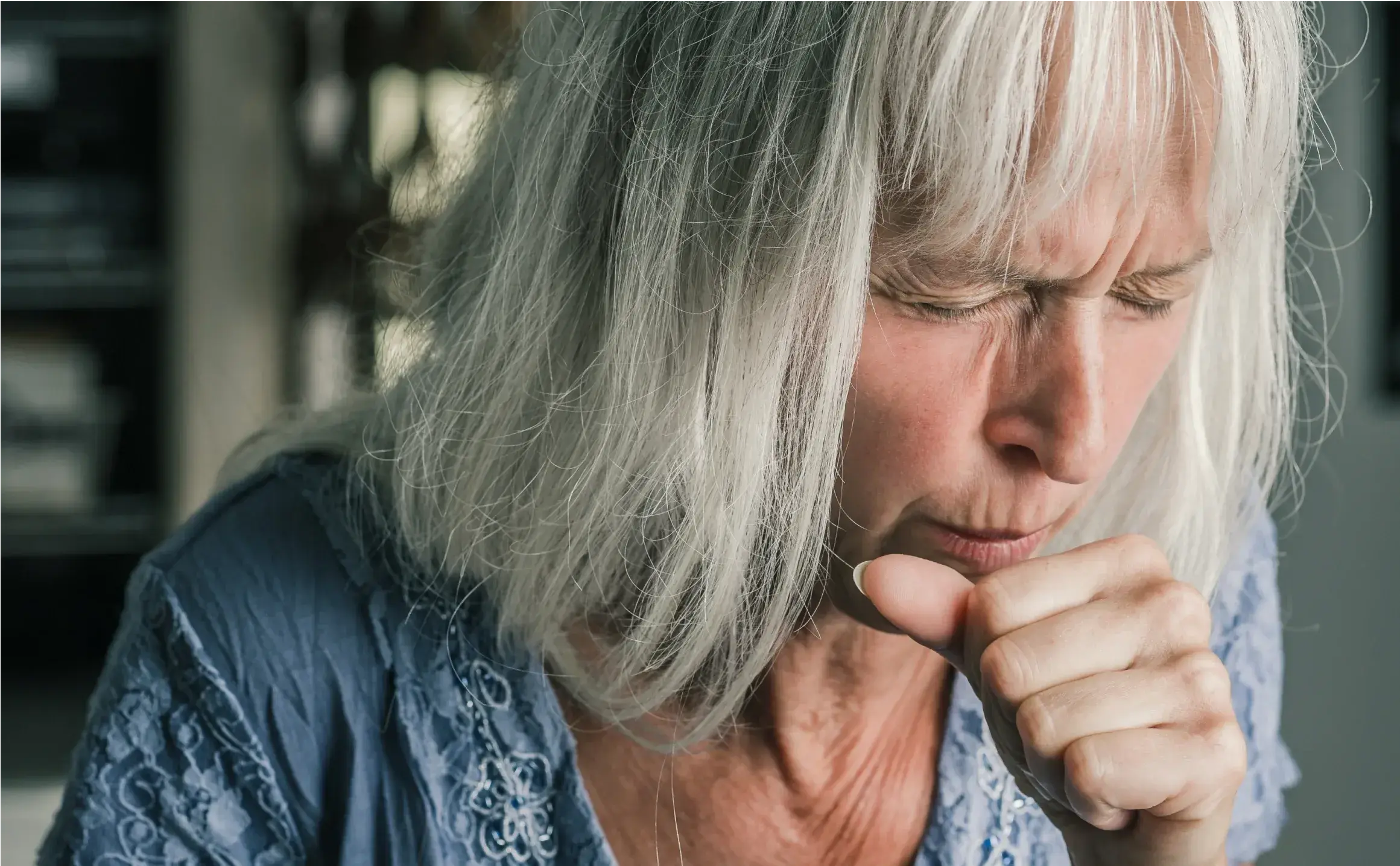 Eine ältere Frau hustet mit schmerzverzerrtem Gesicht in die Hand