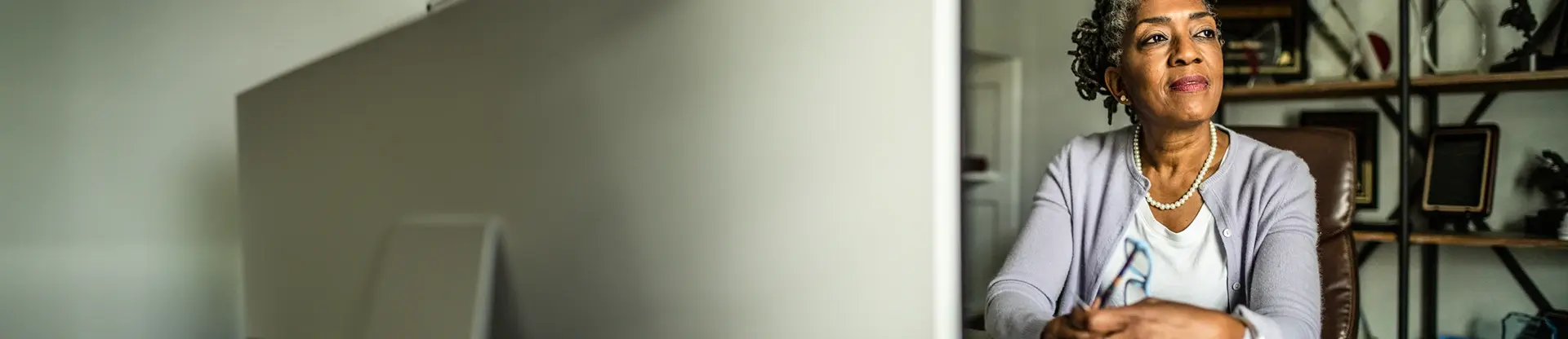 Porträt einer älteren Frau am Computer, die ihren Blick schweifen lässt