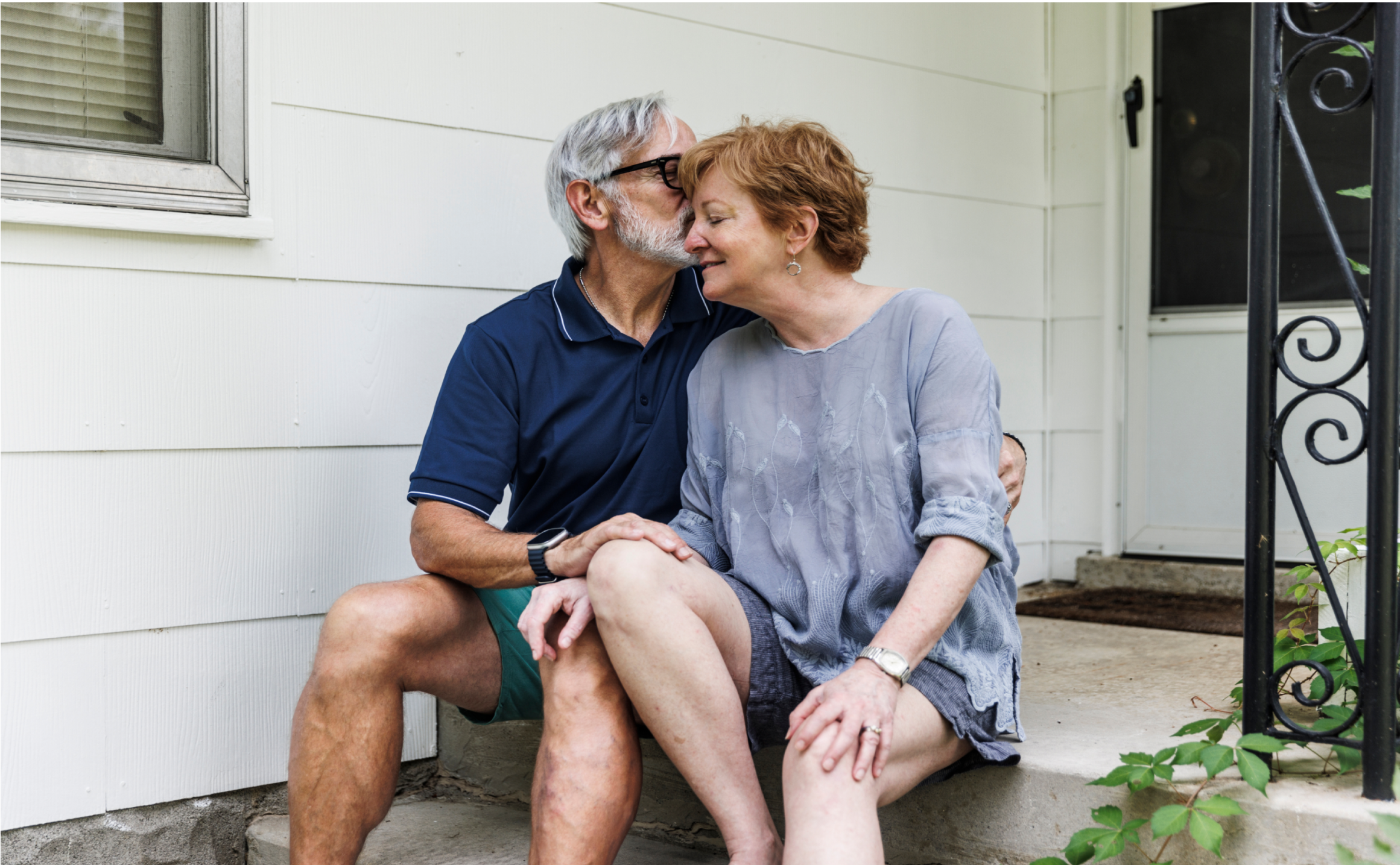 Un couple âgé s’embrasse tendrement en étant assis sur les marches d’un perron.