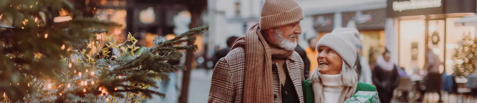 Couple de seniors se promenant en extérieur pendant l'hiver dans un environnement urbain décoré pour les fêtes.
