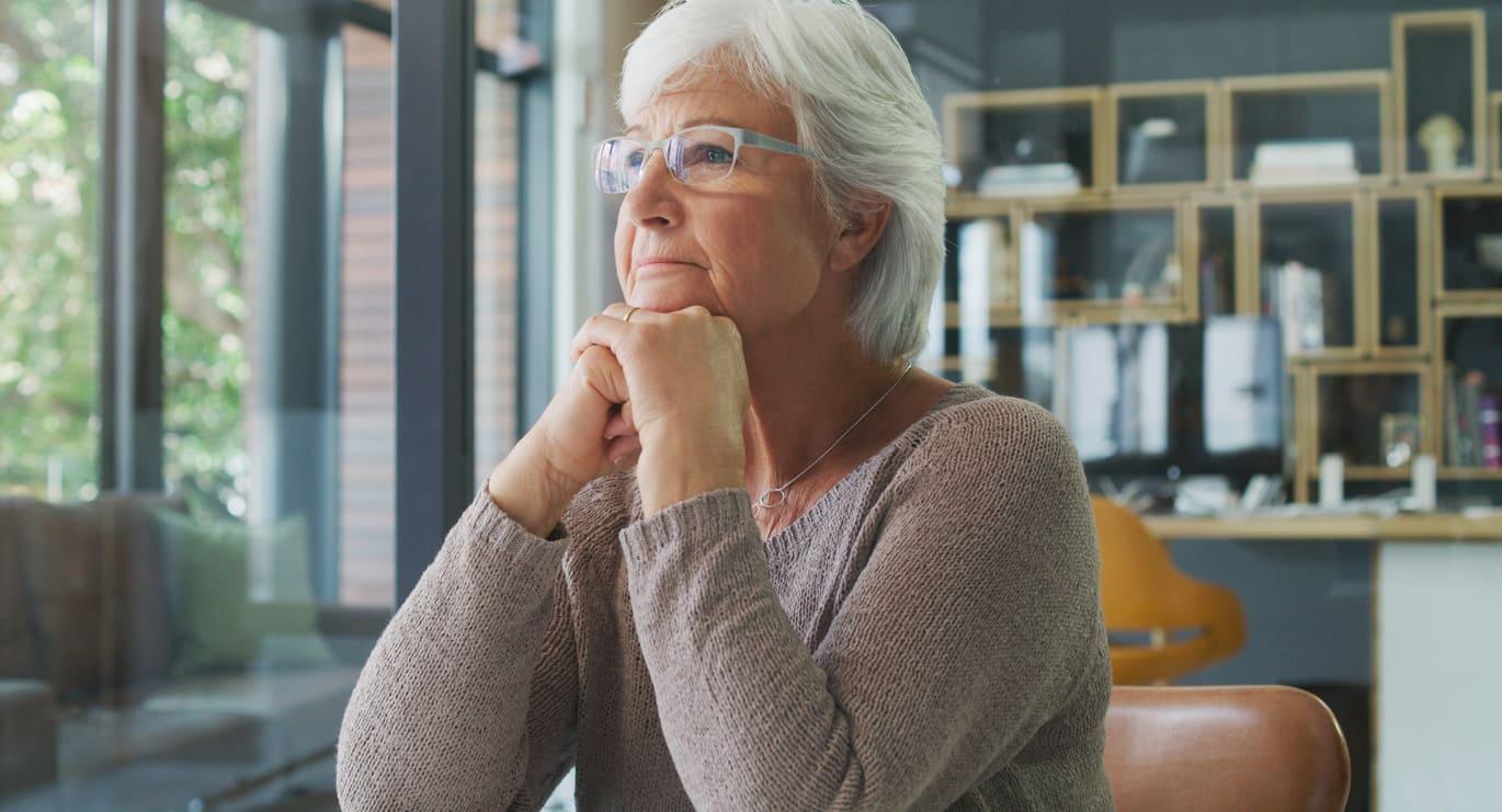 Femme âgée pensive les mains jointes, regardant devant elle